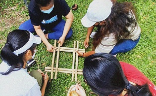 Close up of 4 people making a bamboo craft item together
