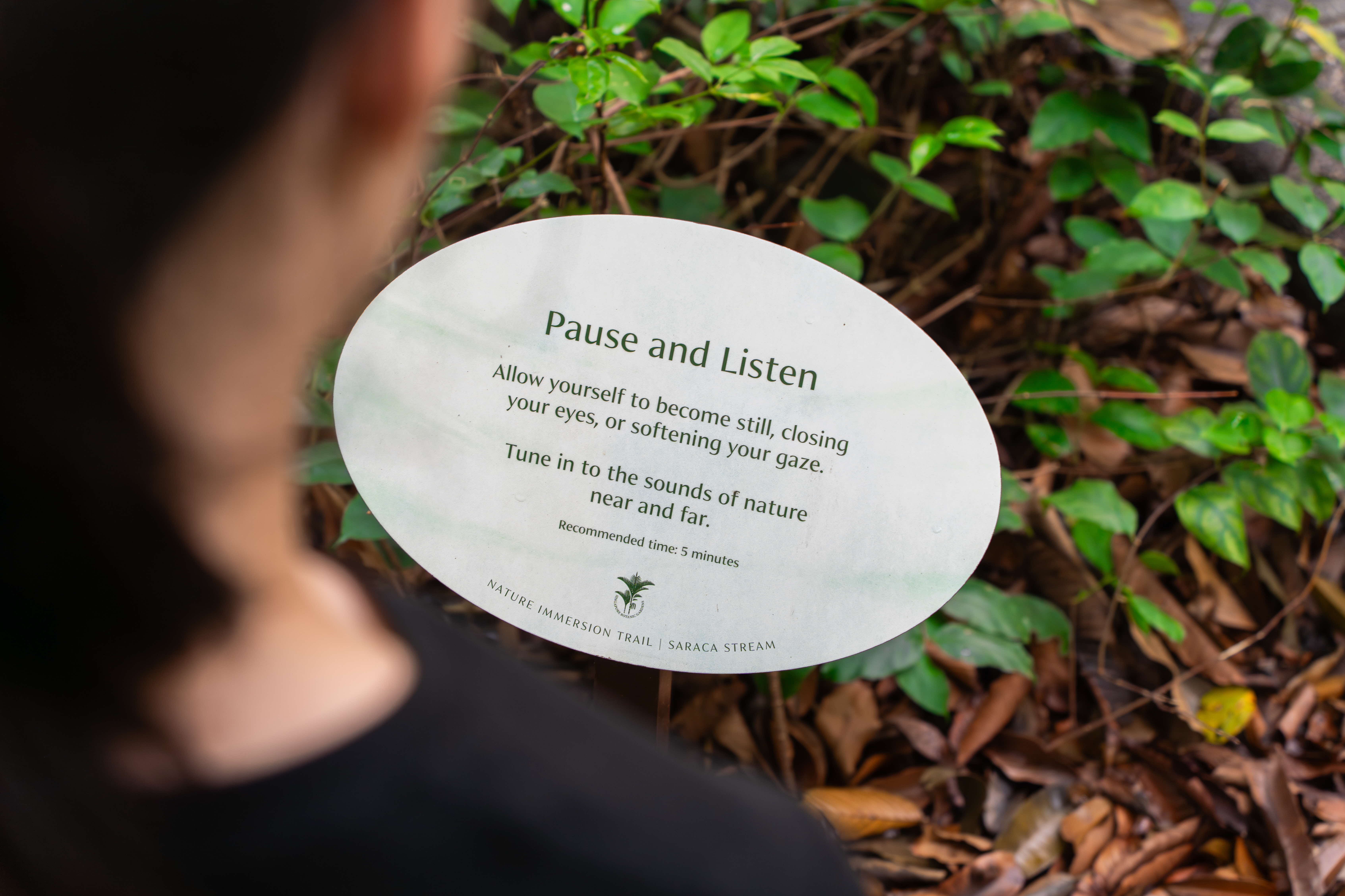 Pause and Listen signboard inviting visitors to become still, close their eyes, and soften their gaze in mindful reflection.