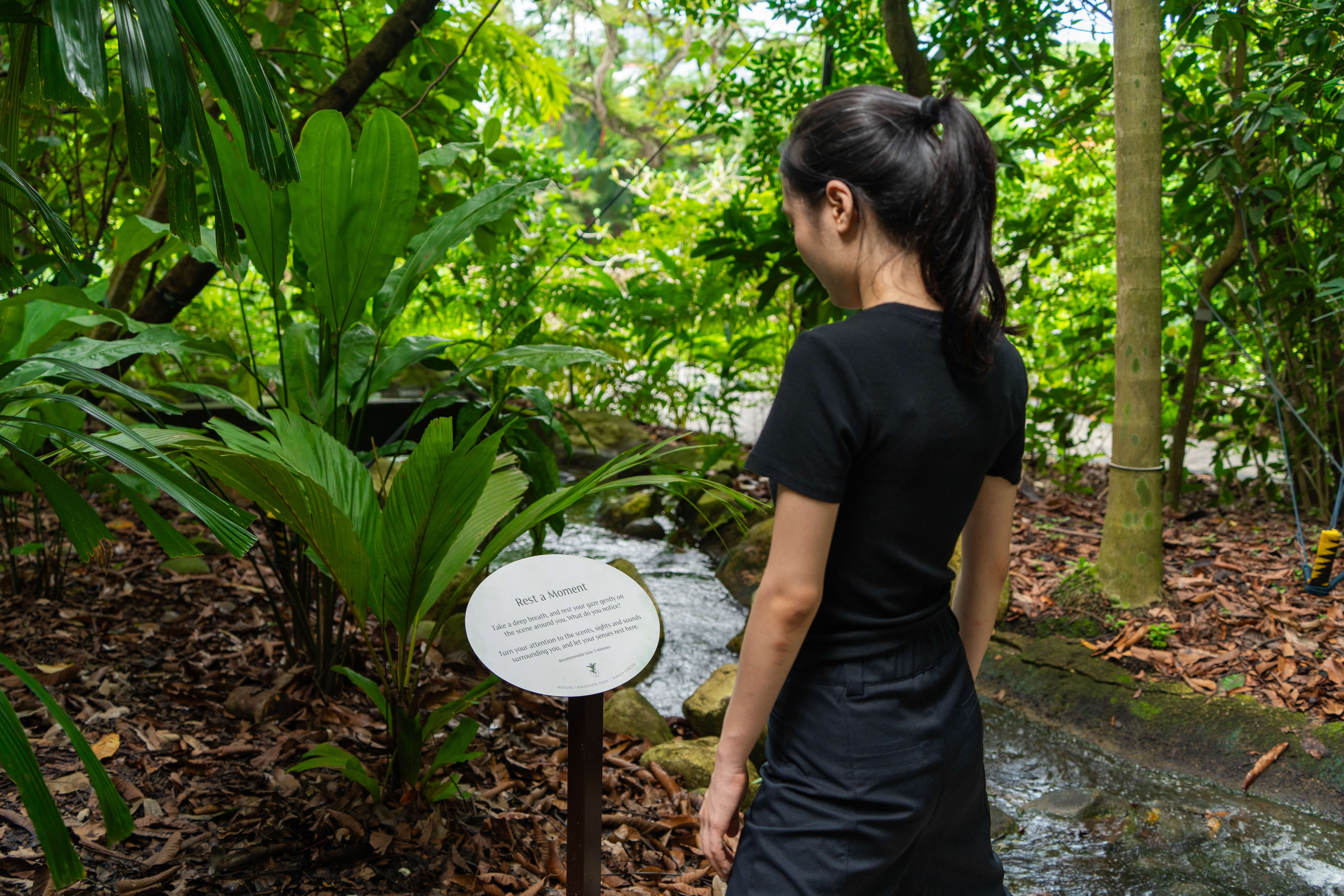 A girl reading the 'Rest for a Moment' signboard along the nature trail.