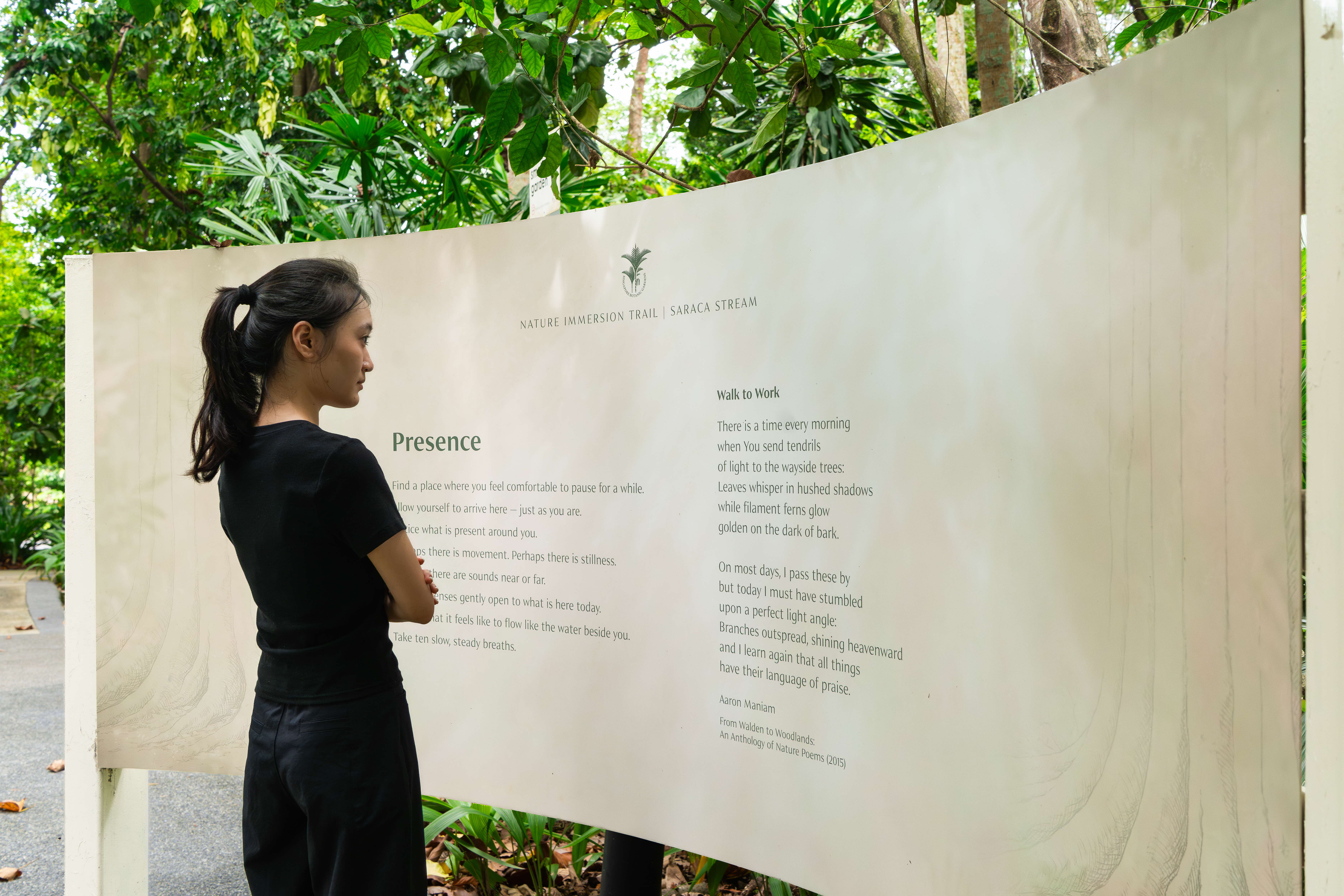 A girl reading a shelter sign displaying the poem 'Walk to Work' by Aaron Maniam, from his nature poetry anthology (2015).